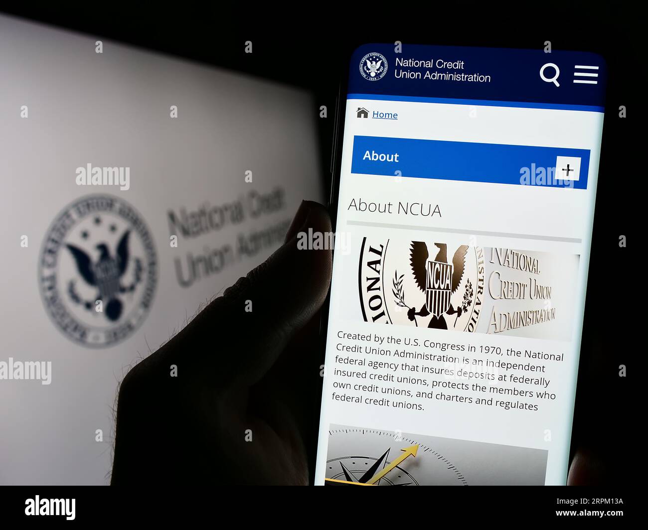 Personne détenant un téléphone cellulaire avec le site Web de la National Credit Union Administration (NCUA) sur l'écran devant le sceau. Concentrez-vous sur le centre de l'écran du téléphone. Banque D'Images