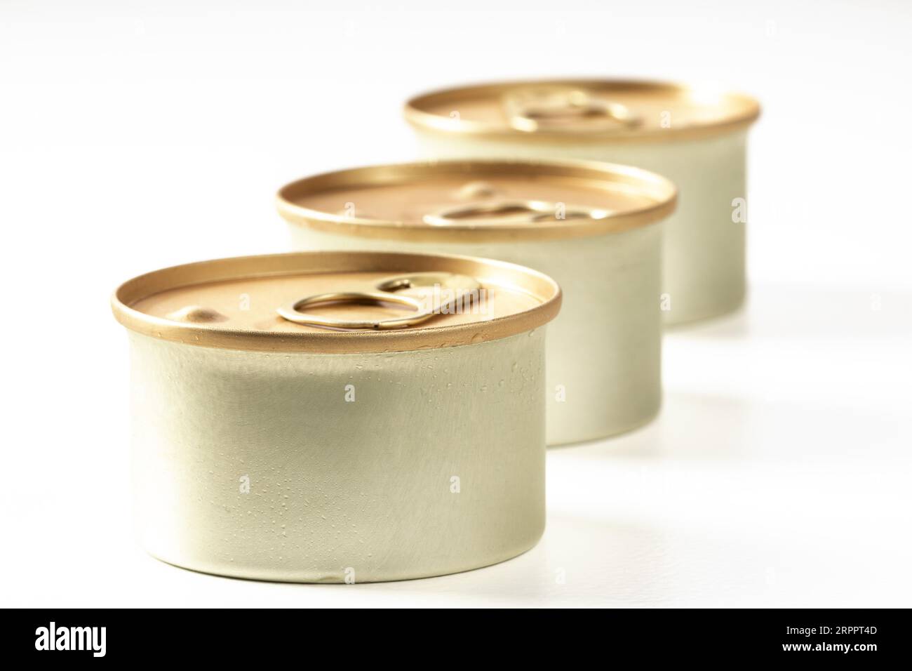 Trois pots métalliques de nourriture pour chat sont disposés en diagonale sur un fond blanc. Il y a des gouttes de condensation sur les bocaux, ils ont été juste sortis de t Banque D'Images