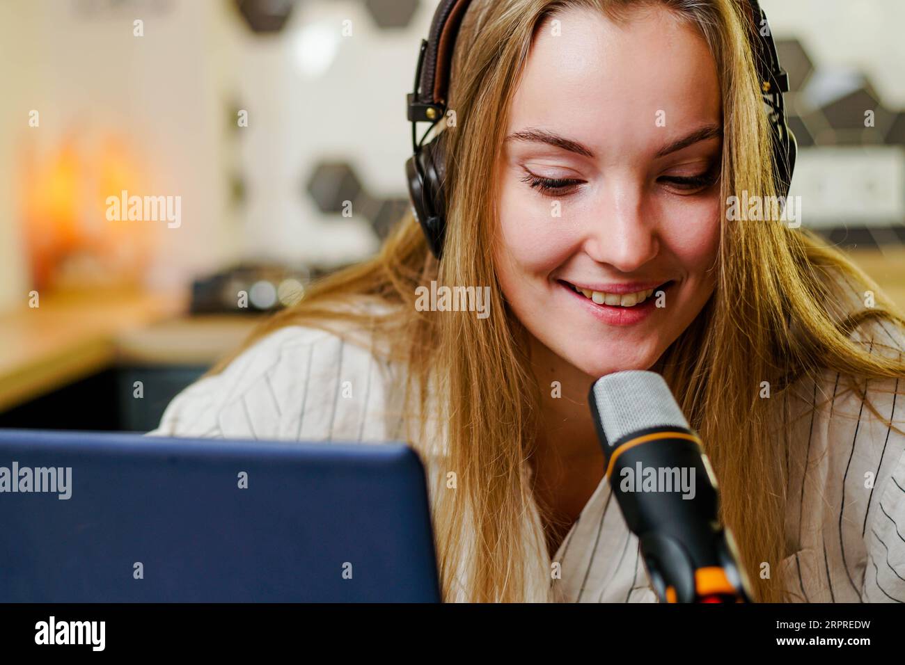 Jeune femme souriante avec des écouteurs enregistrant podcast à l'aide d'un ordinateur portable au home studio, diffusant une interview à l'aide d'un microphone. Banque D'Images