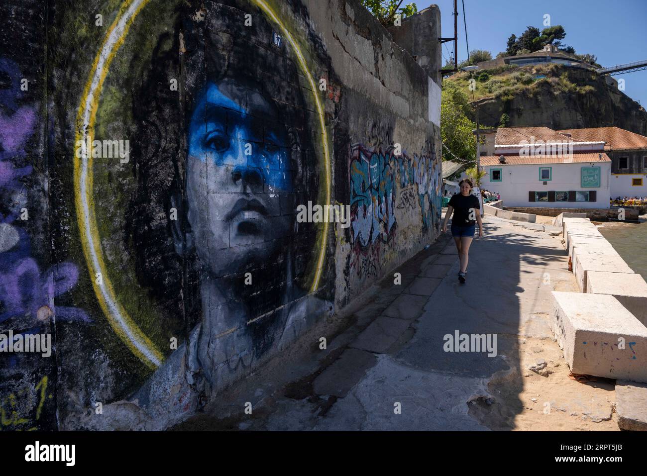 Une femme vue marchant près d'un mur avec l'image du joueur de football Diego Maradona, dans la ville d'Almada. Situé sur la rive sud du fleuve Tejo, Almada est le meilleur point de vue sur la ville de Lisbonne, avec le château, l'ascenseur panoramique de Boca do Vento et la statue du Christ Roi construite en 1959, ils sont utilisés comme points d'observation. Banque D'Images