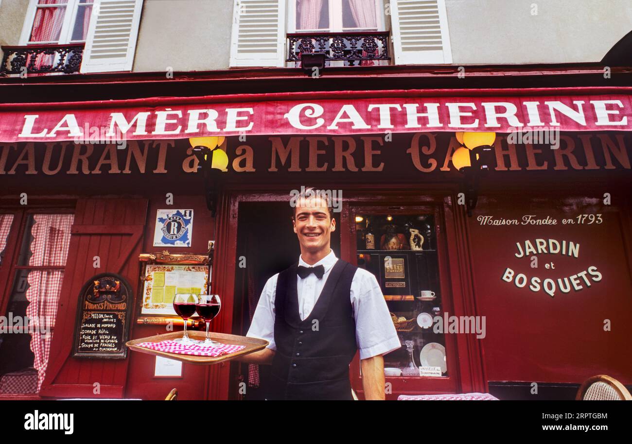 Serviteur français style rétro MONTMARTRE en uniforme noir et blanc traditionnel typique avec noeud papillon, servant des verres à vin rouge en plein air sur plateau au célèbre restaurant Montmartre boulevard la Mere Catherine Paris France Banque D'Images