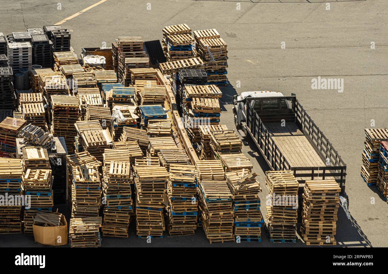 San Francisco, CA, USA - 13 juillet 2023 : après le chargement d'un navire, piles de palettes en bois vides jaunes ou bleues dans le port au quai. Camion prêt à en charger Banque D'Images
