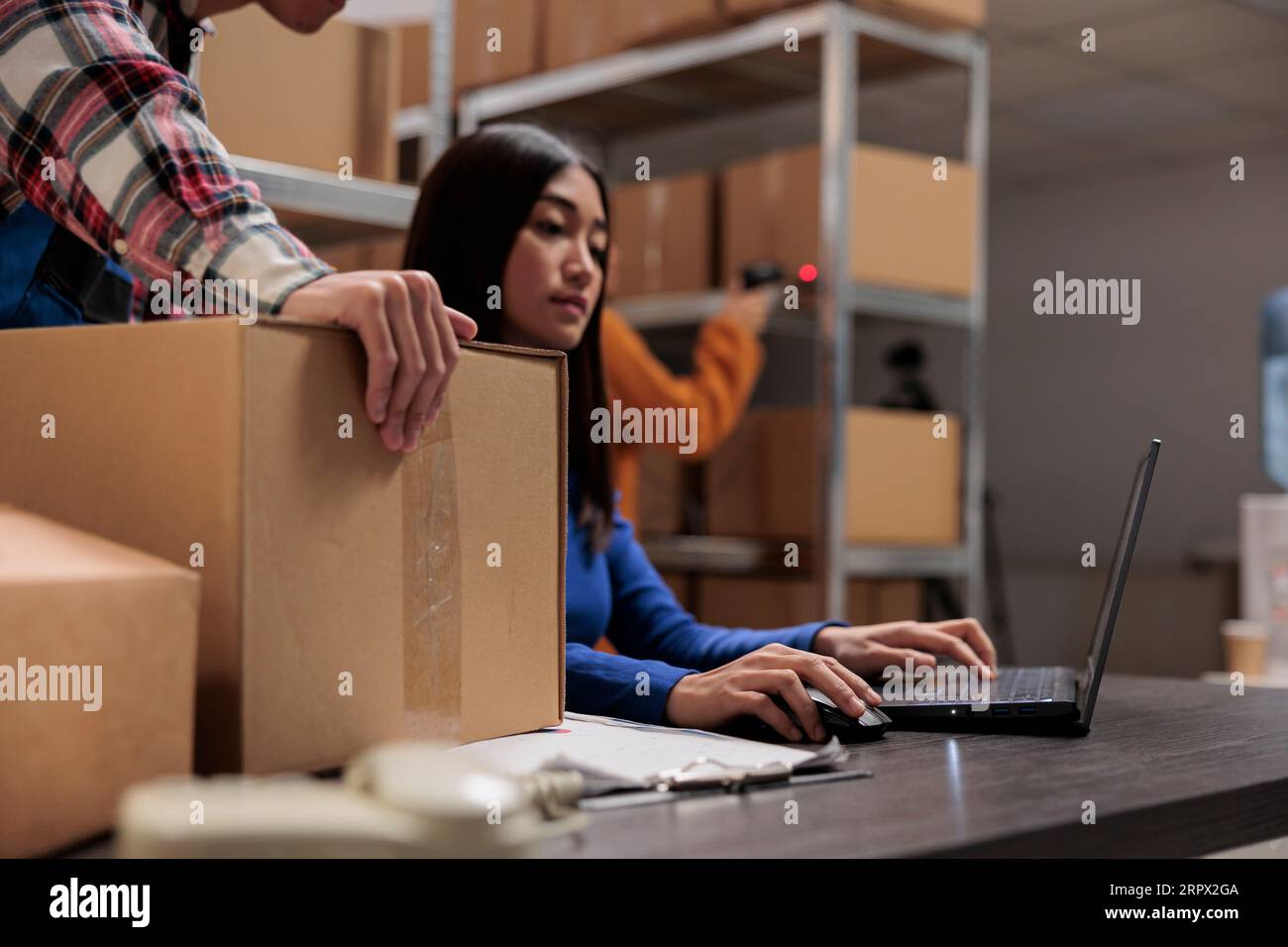 Les travailleurs de l'entrepôt préparent le colis pour la livraison et analysent les commandes sur ordinateur portable tout en travaillant au bureau de la salle de stockage. Les employés de Storehouse coopèrent pour gérer l'expédition de boîtes en carton Banque D'Images