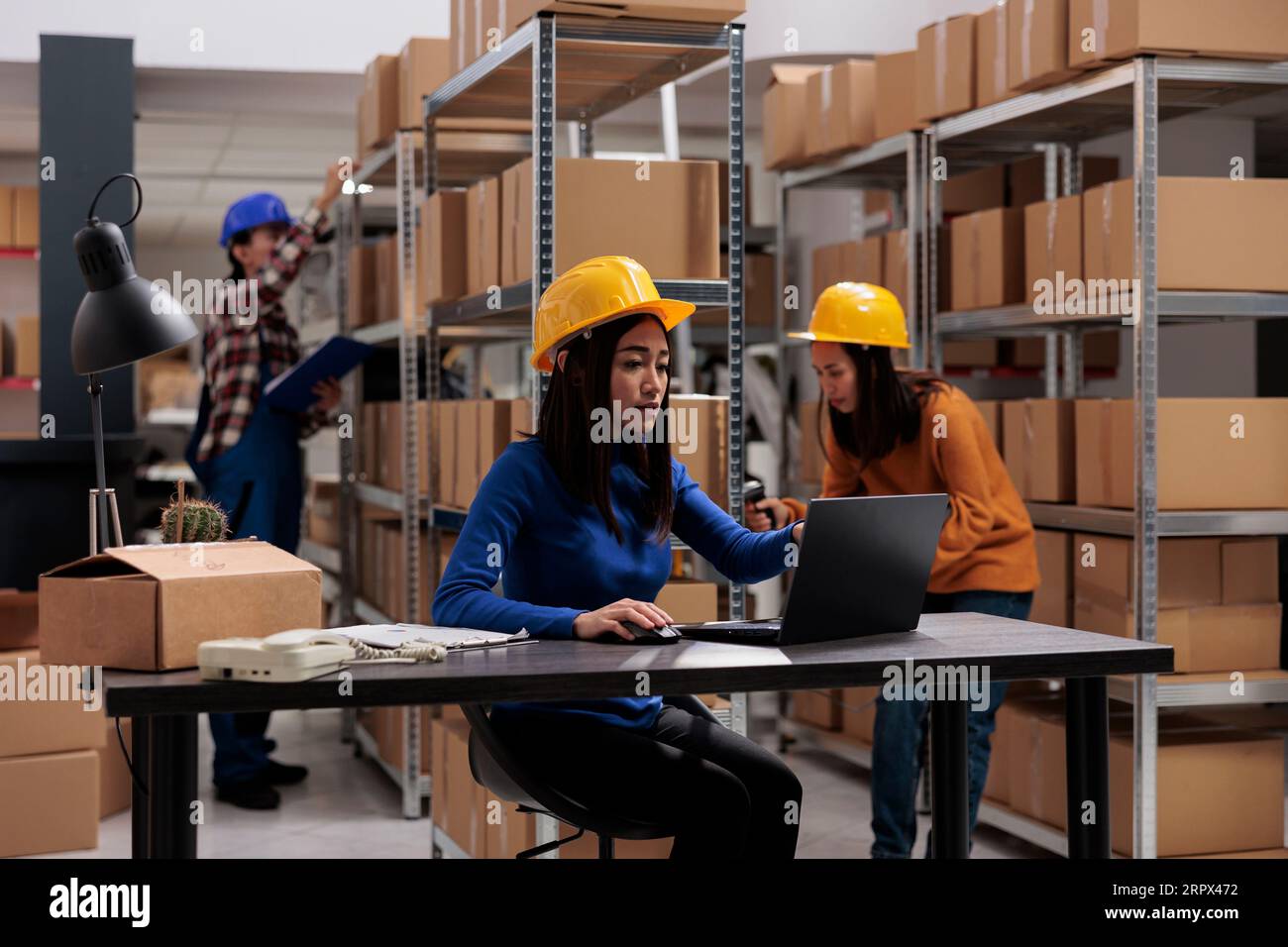 Préparateur de commande d'entrepôt vérifiant le ticket de prélèvement sur l'ordinateur portable pour préparer le colis du client pour la livraison. Jeune ouvrier asiatique de magasin dans le casque jaune analysant les marchandises en stock sur ordinateur Banque D'Images