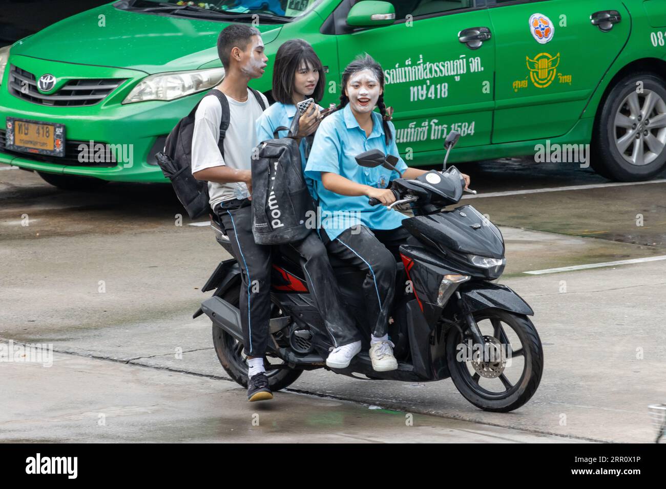 SAMUT PRAKAN, THAÏLANDE, JUIN 06 2023, Un trio d'adolescents avec de la poudre sur le visage roulent une moto sous la pluie Banque D'Images