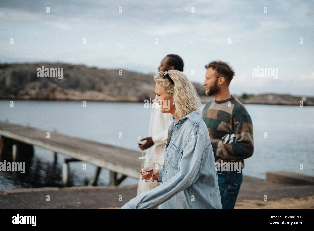 Vue latérale de la jeune femme appréciant des boissons tout en marchant avec des amis près du lac Banque D'Images