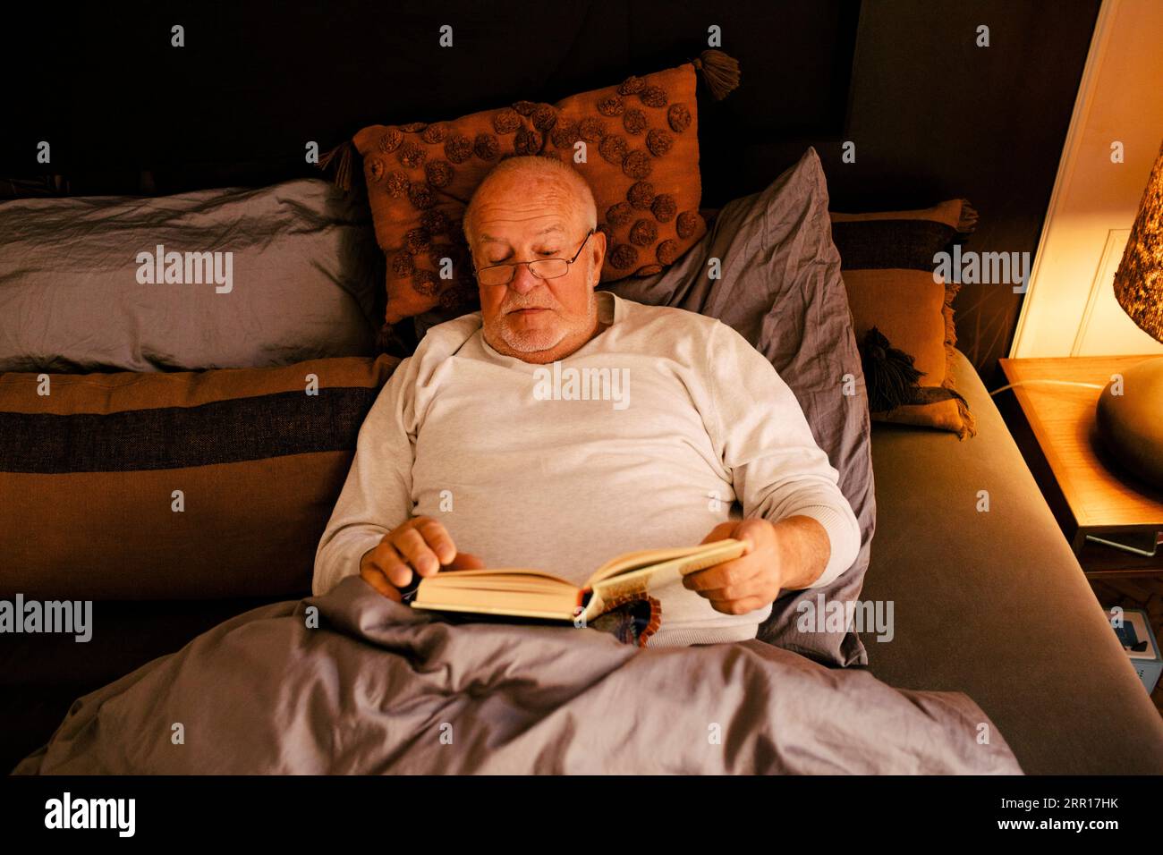 Homme senior lisant le livre tout en étant allongé sur le lit à la maison Banque D'Images