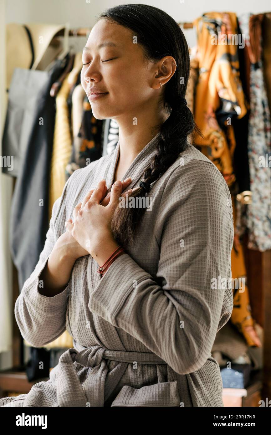 Jeune femme avec les mains sur la poitrine méditant à la maison Banque D'Images