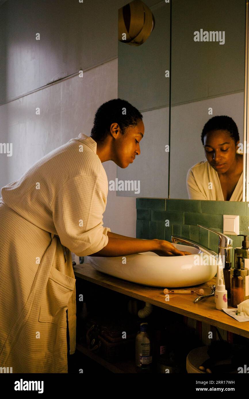 Vue latérale de la jeune femme laver le savon à l'évier dans la salle de bains Banque D'Images