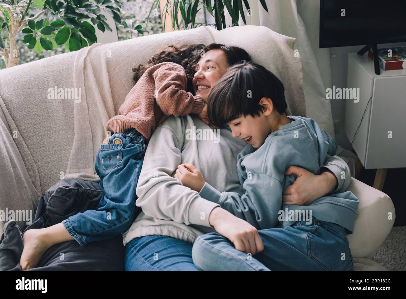 Garçon et fille ludiques avec la mère sur le canapé à la maison Banque D'Images