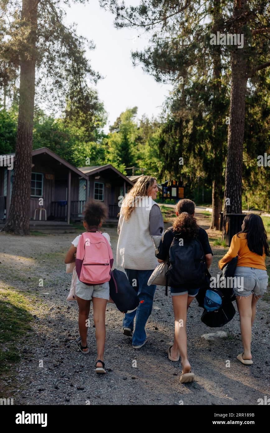 Vue arrière du conseiller de camp marchant avec les filles sur le sentier au camp d'été Banque D'Images