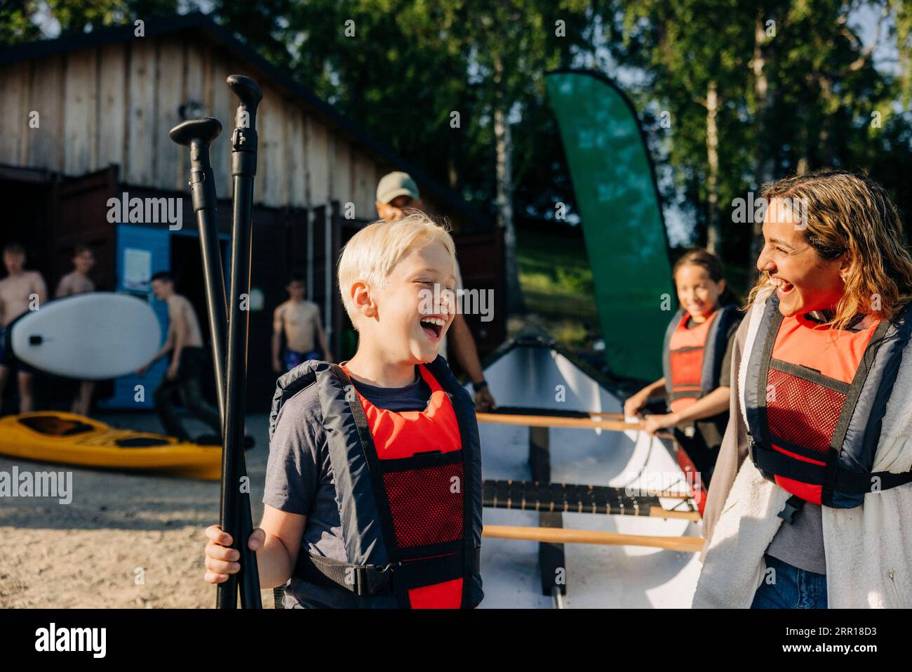 Garçon heureux avec conseiller portant des gilets de sauvetage tout en allant faire du kayak au camp d'été Banque D'Images