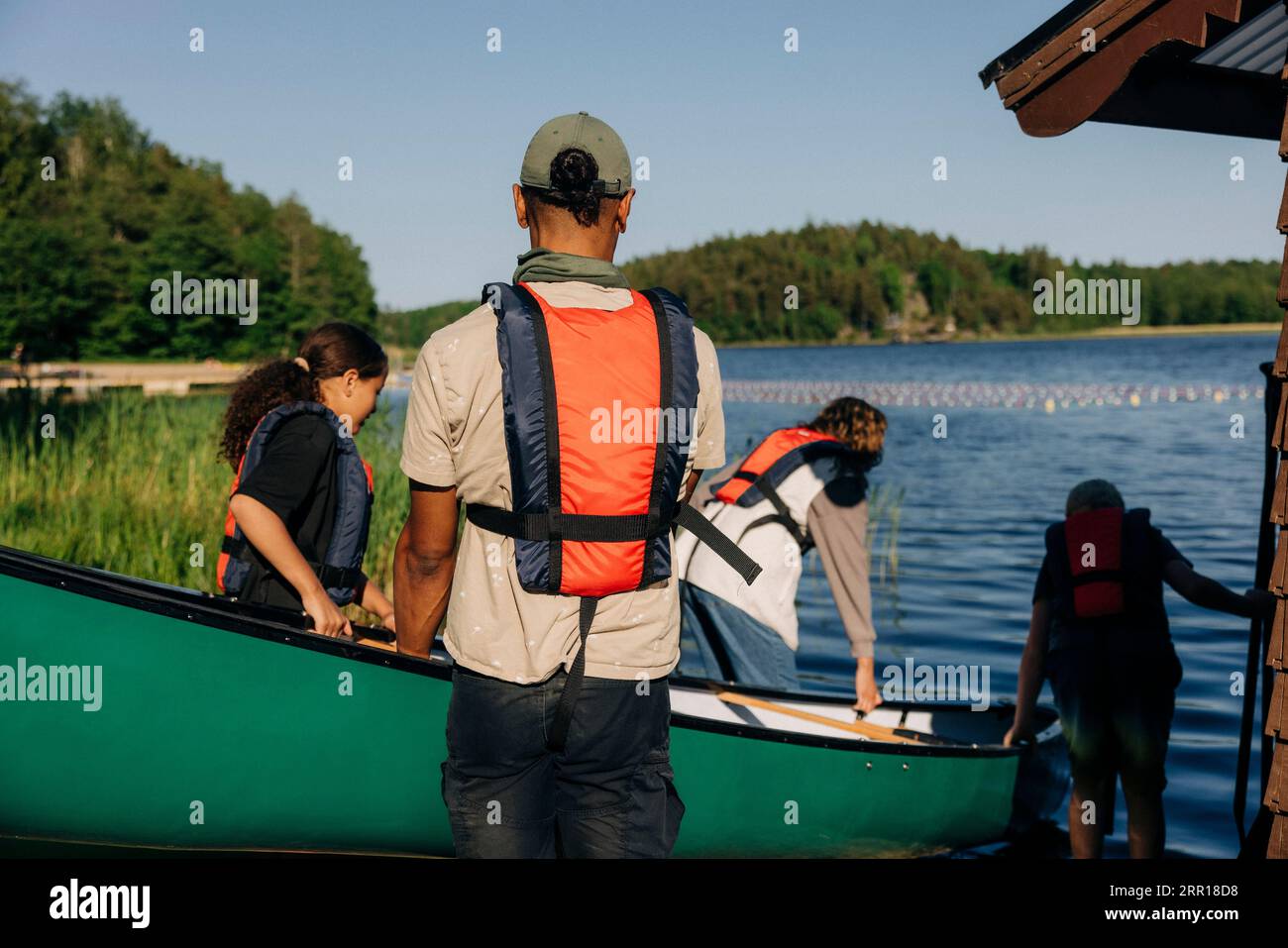 Vue arrière du conseiller masculin allant faire du kayak avec des enfants au camp d'été Banque D'Images