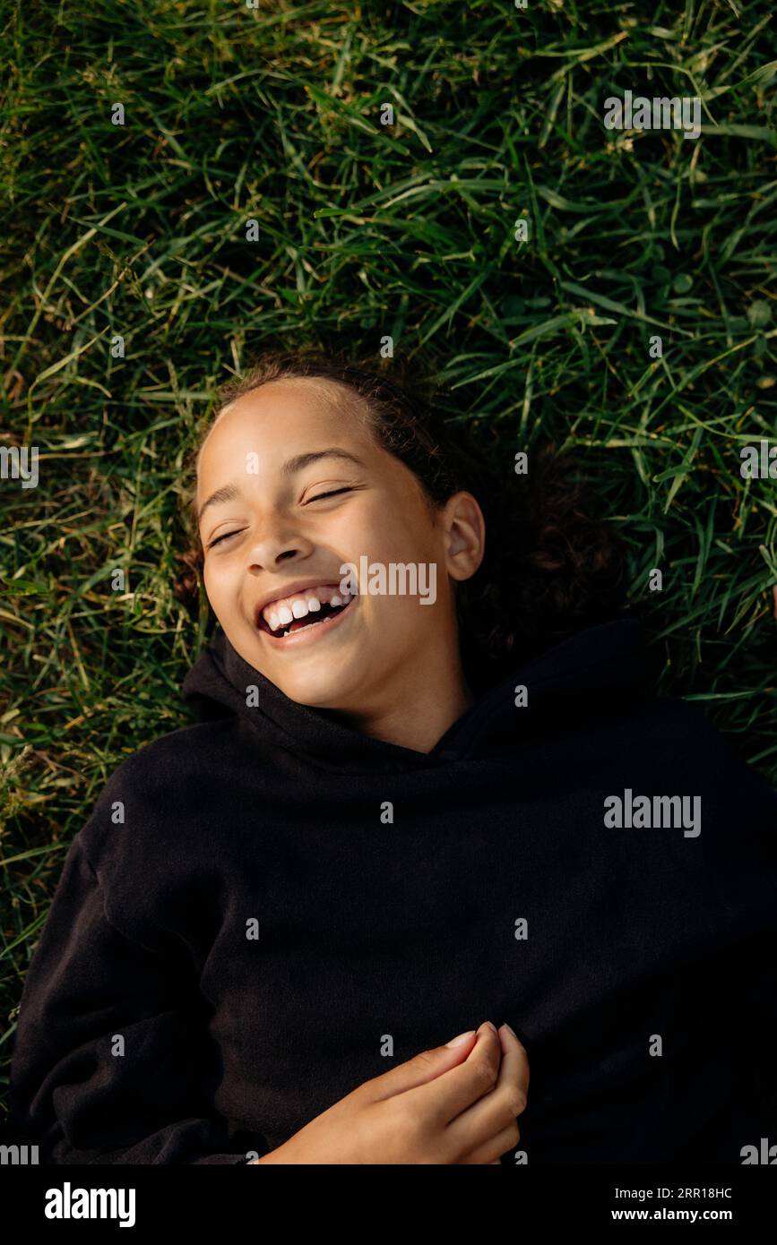 Directement au-dessus plan de fille insouciante riant tout en s'allongeant sur l'herbe au camp d'été Banque D'Images