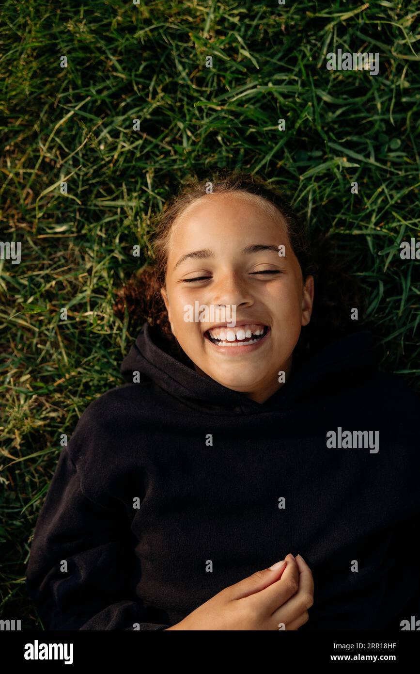 Fille heureuse riant en s'allongeant sur l'herbe au camp d'été Banque D'Images