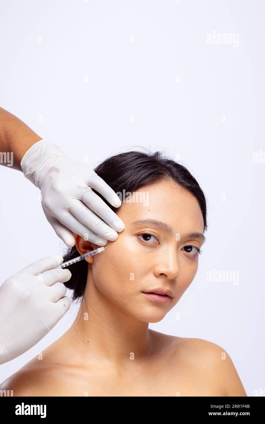 Mains d'esthéticienne en gants chirurgicaux blancs injectant du botox dans la joue d'une femme asiatique, espace copie Banque D'Images