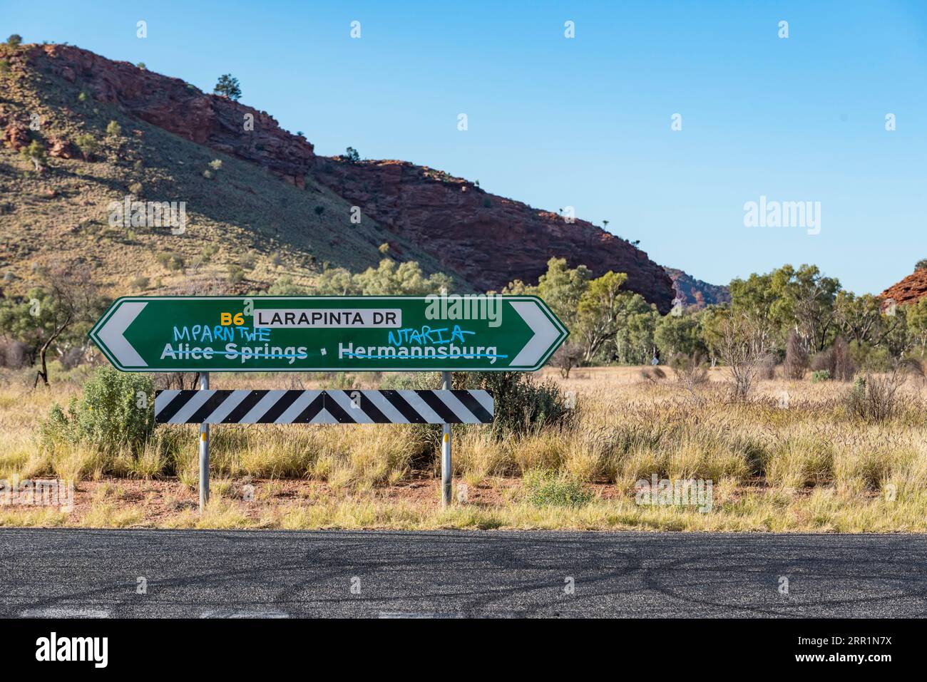 Un panneau routier avec les noms d'Alice Springs et Hermannsburg barré et pulvérisé au-dessus avec le nom aborigène local Arrernte Mparlwe et Ntaria Banque D'Images