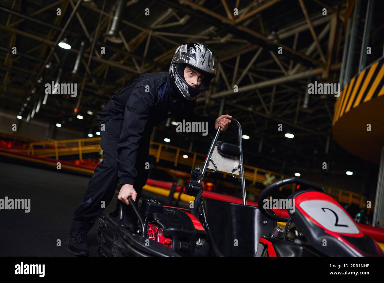 motorsport et speed drive, pilote de kart concentré en casque et sportswear poussant le kart sur circuit Banque D'Images