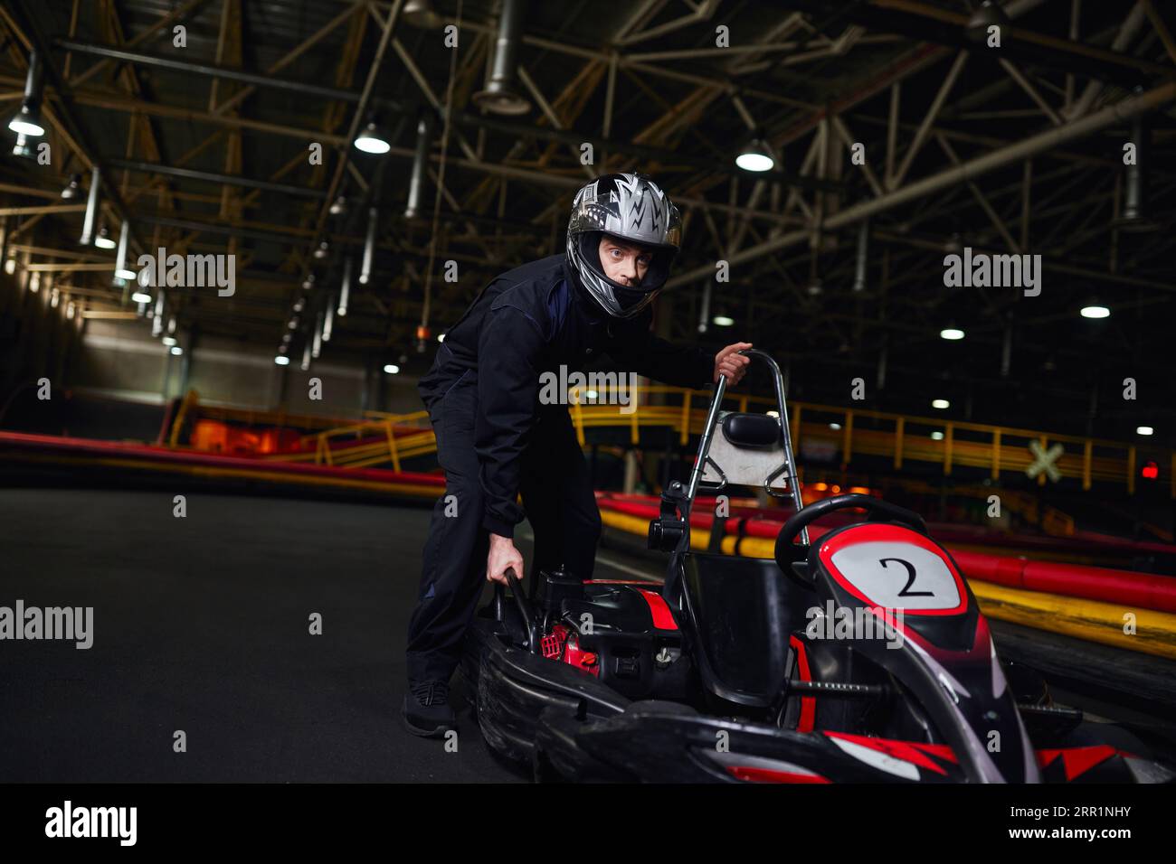 motorsport et speed drive, pilote de kart concentré en sportswear et casque poussant le kart sur circuit Banque D'Images