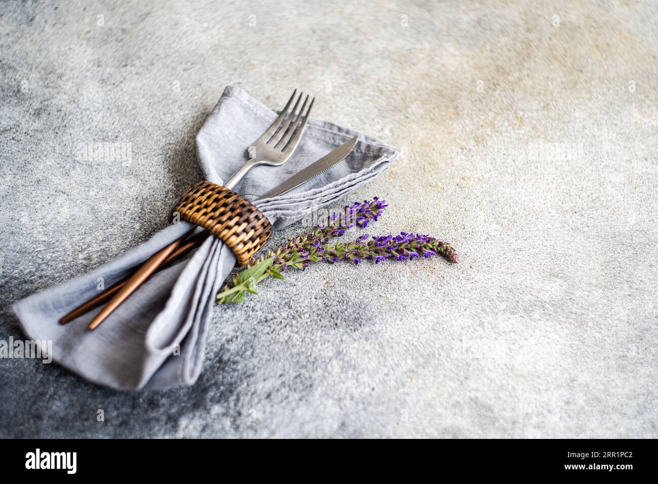 Angle élevé de réglage de table avec couverts argentés, serviette et fleurs de lavande sur fond gris flou Banque D'Images