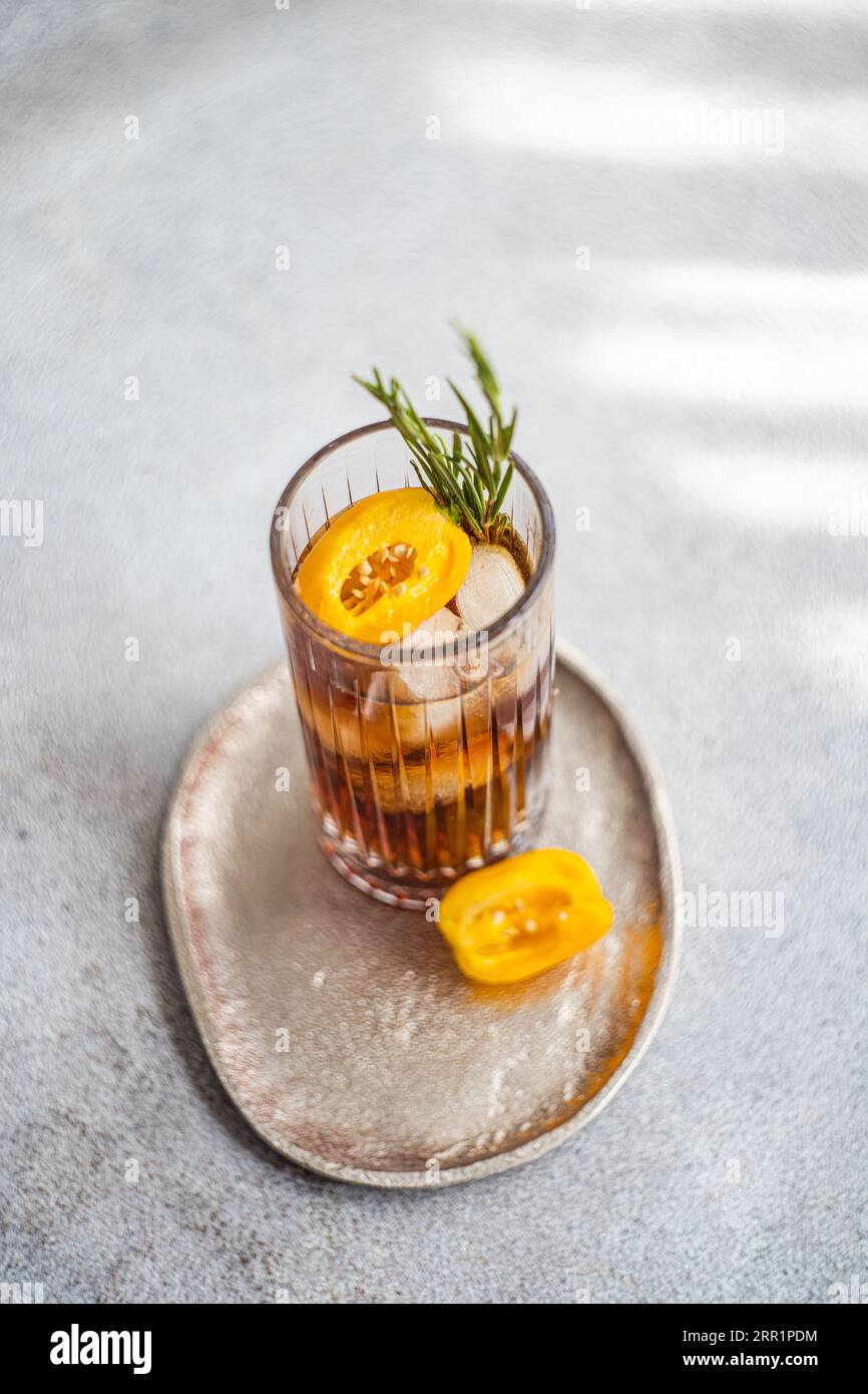 Angle élevé de cocktail Margarita épicé servi avec des glaçons et des tranches de fruits frais placés sur un plateau sur fond gris Banque D'Images