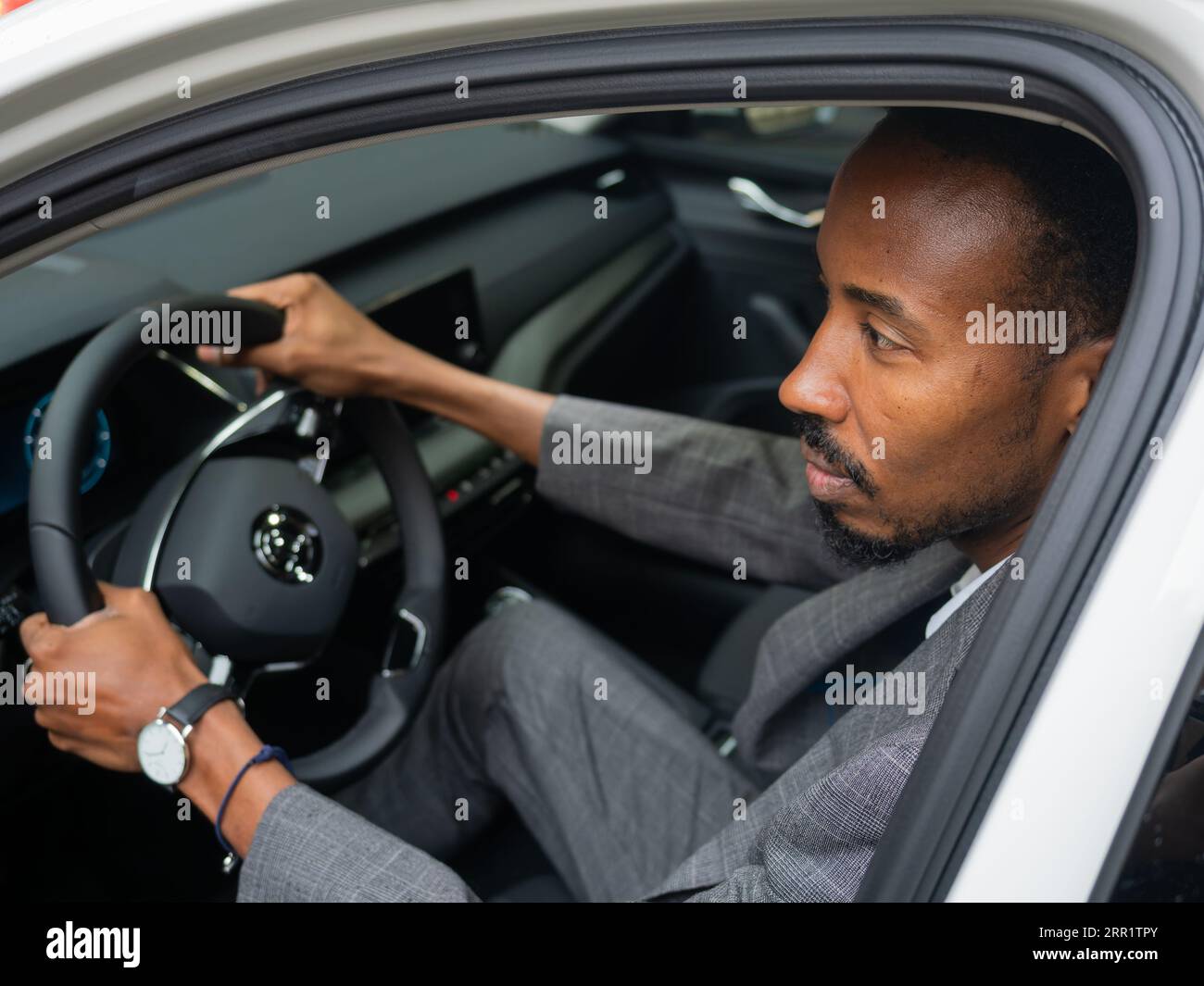 D'en haut d'un jeune homme afro-américain souriant regardant loin tout en étant assis dans le siège du conducteur avec la porte ouverte avec le verre de fenêtre réfléchissant à la lumière du jour Banque D'Images