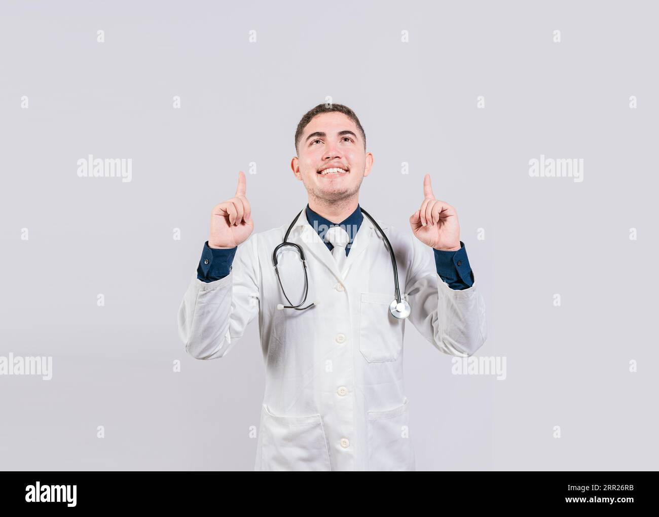 Beau docteur pointant une publicité vers le haut. Docteur heureux regardant et pointant vers le haut isolé. Médecin souriant pointant une promo vers le haut Banque D'Images