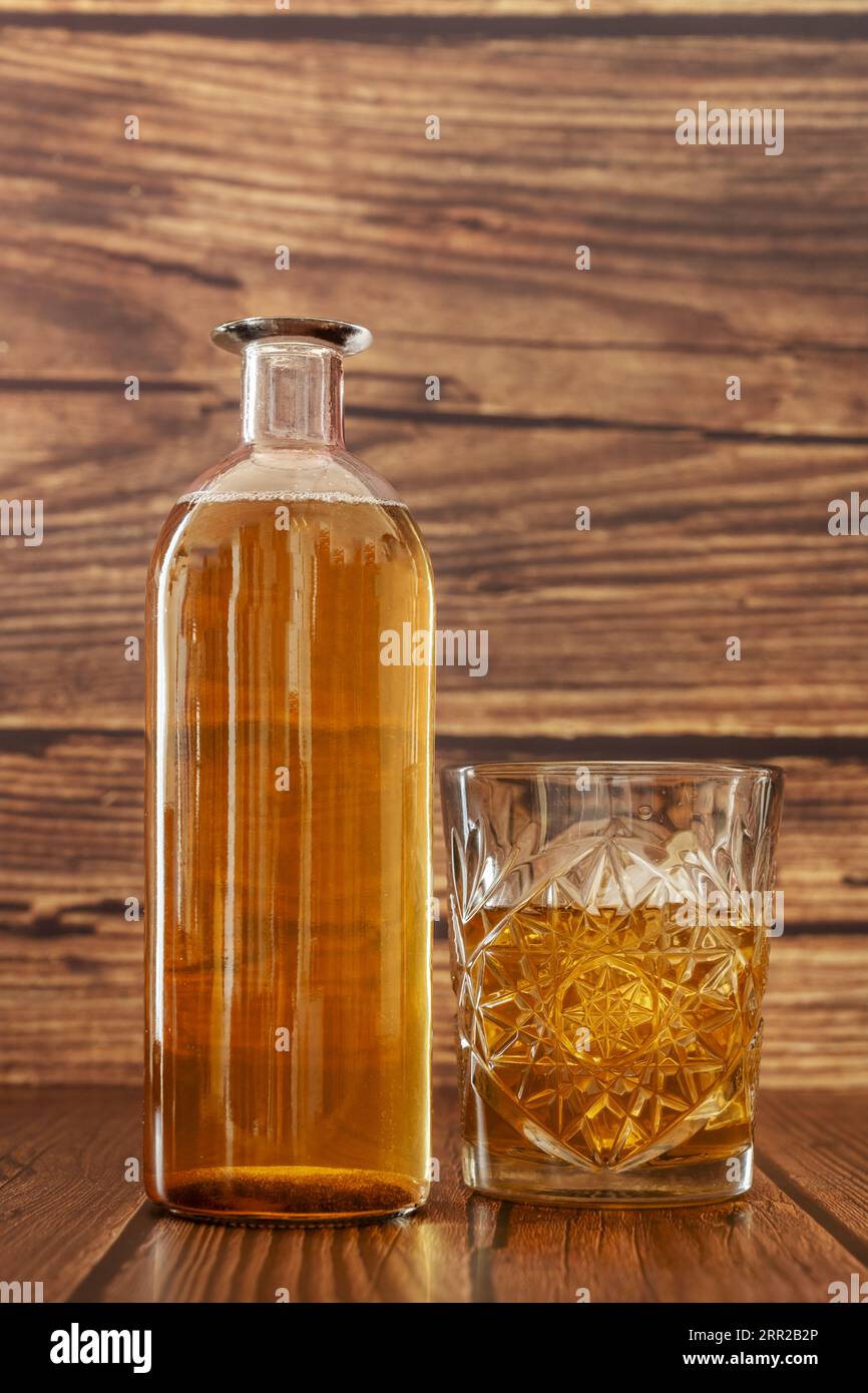 Une bouteille et un verre sculpté remplis d'une liqueur d'ambre entourés de surfaces en bois sombre Banque D'Images
