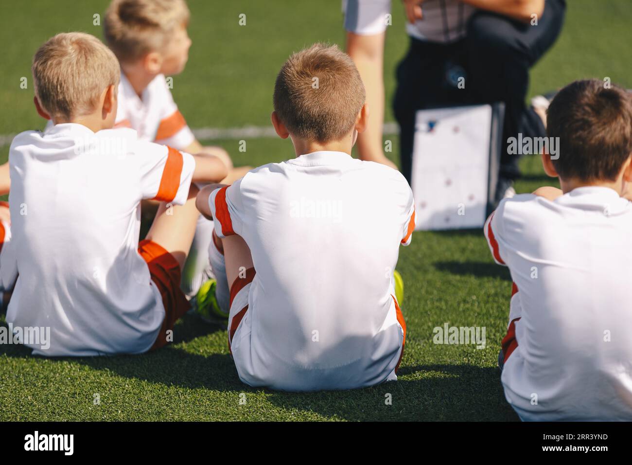 Enfants garçons sur l'entraînement de football avec un entraîneur. Le formateur explique les tactiques à l'aide du tableau blanc stratégique. Garçons écoutant l'entraîneur à la pratique de football Banque D'Images