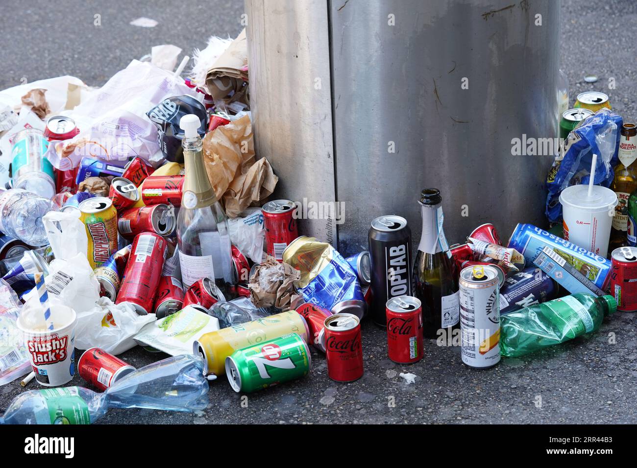 Nourriture et déchets de bouteilles vides dans et autour de la poubelle publique dans la rue. Banque D'Images