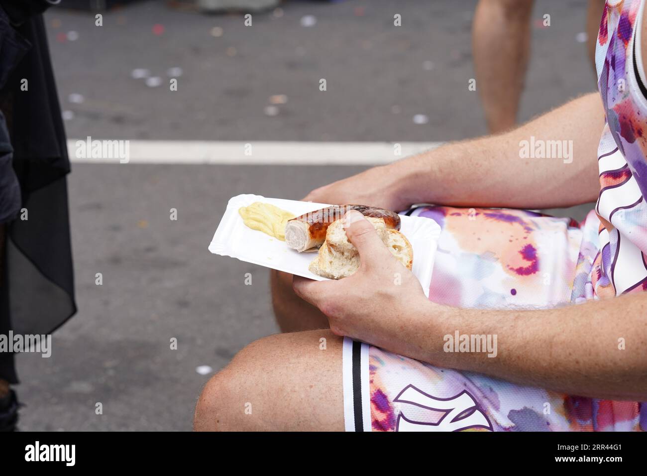 Homme assis tenant une saucisse suisse grillée et du pain sur un plateau de papier Découpe d'une personne ayant du repos et prenant un repas de restauration rapide. Banque D'Images