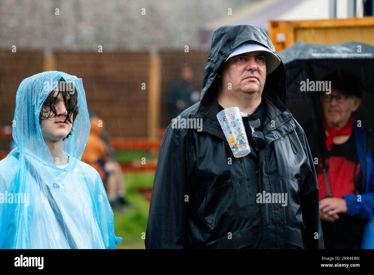 Adolescent dans un poncho jetable de pluie et un homme avec un verre de bière dans la pluie. Green Man Festival, Brecon, pays de Galles, Royaume-Uni, 2023. Photo : Rob Watkins Banque D'Images