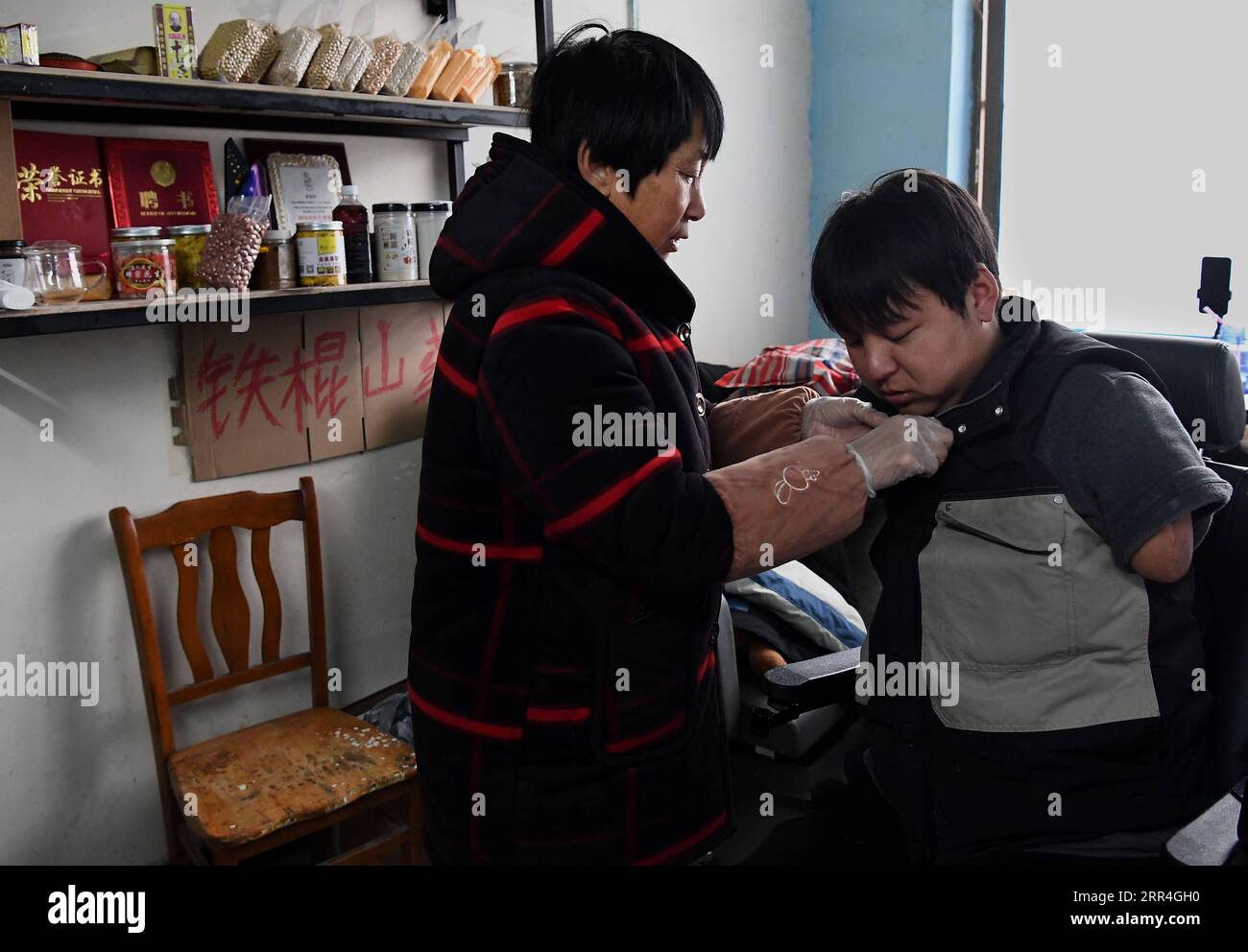 201204 -- ZHENGZHOU, 4 décembre 2020 -- la mère de Sun Yahui l'aide à s'habiller à la maison dans le village de Yangzhuang à Xinxiang, dans la province du Henan au centre de la Chine, le 2 décembre 2020. Salut, tout le monde aujourd'hui je vais vous montrer comment creuser des racines de lotus dans le village de mon oncle. Alors qu'un nouveau jour commençait, Sun Yahui prépara le téléphone portable avec son membre gauche et commença son livestreaming. Sun Yahui, 26 ans, a perdu ses deux bras et a été paralysé à cause d'une blessure électrique il y a 4 ans. Je pensais que j'étais inutile. L'accident a laissé des blessures sur son corps et des cicatrices émotionnelles sur son esprit. Pour soigner ses blessures, les parents de Sun ont dépensé toutes les économies et borrowe Banque D'Images