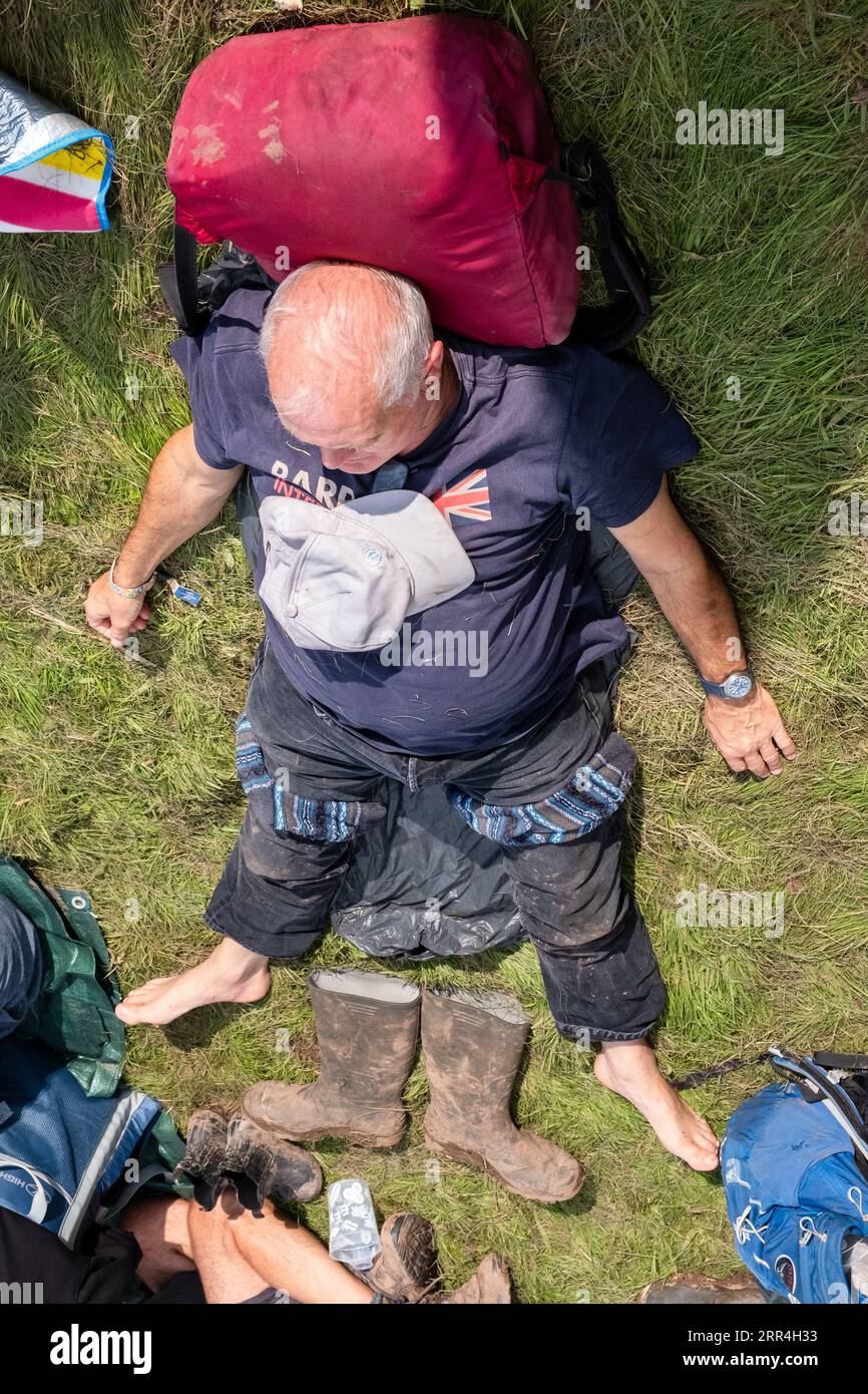 Un homme âgé d'âge moyen fait une sieste au soleil et pose ses bottes boueuses sur l'herbe au Green Man Festival, Brecon, pays de Galles, Royaume-Uni, 2023. Photo : Rob Wat Banque D'Images