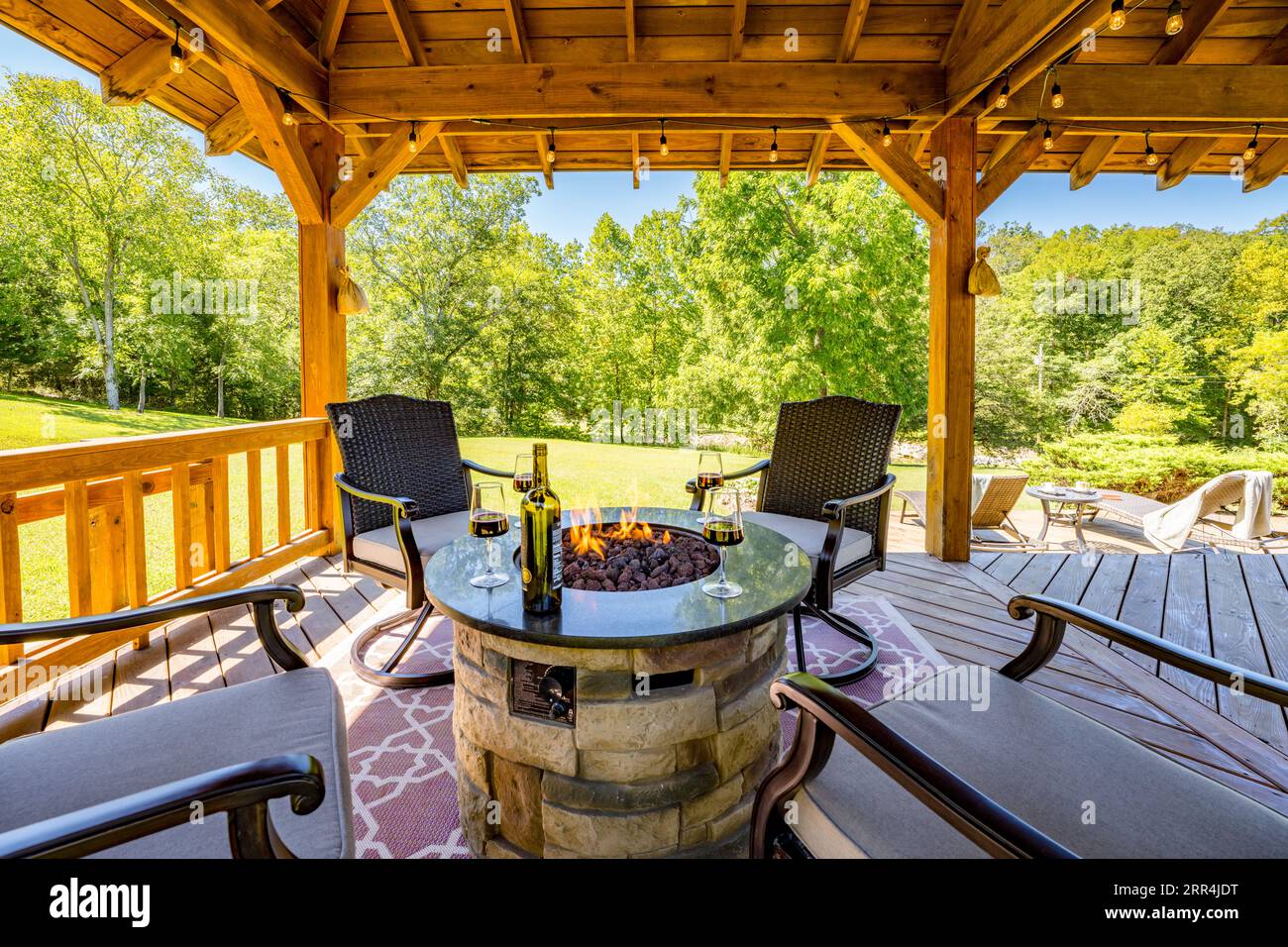 Une scène de vie en plein air avec quatre chaises entourant un foyer sous un pavillon dans une maison de campagne. Une bouteille de vin et des verres à pied sont assis autour du feu. Banque D'Images