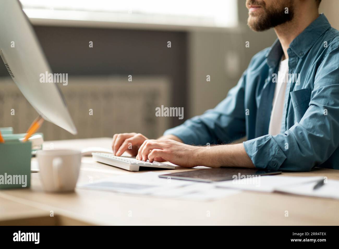 Jeune homme barbu assis au bureau et tapant sur le clavier de l'ordinateur Banque D'Images