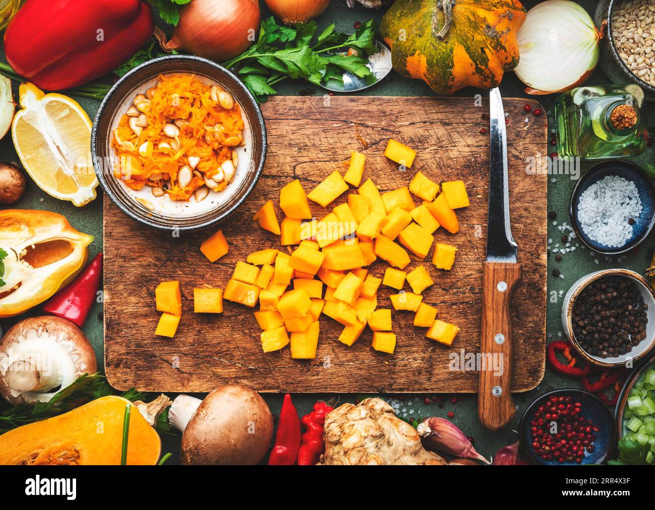 Fond alimentaire. Couteau de citrouille pelée crue en dés et légumes sur une planche à découper en bois rustique. Légumes, champignons, racines, épices - ingrédients pour v Banque D'Images