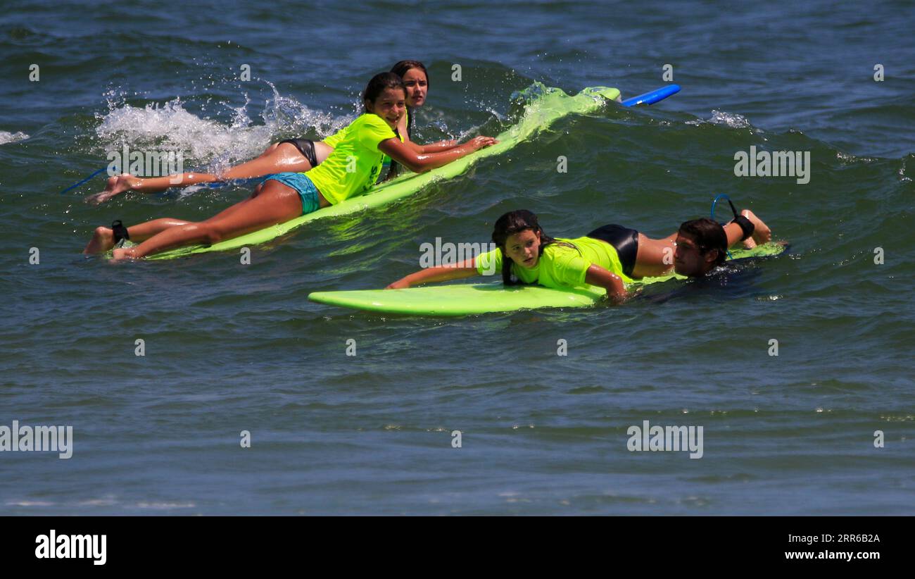 Gilgo Beach, New York, États-Unis - 25 juillet 2023 : enfants en chemises vertes fluo chevauchant sur les vagues tout en surfant au Bunger Surf Camp à Gilgo Beach sur long Island. Banque D'Images