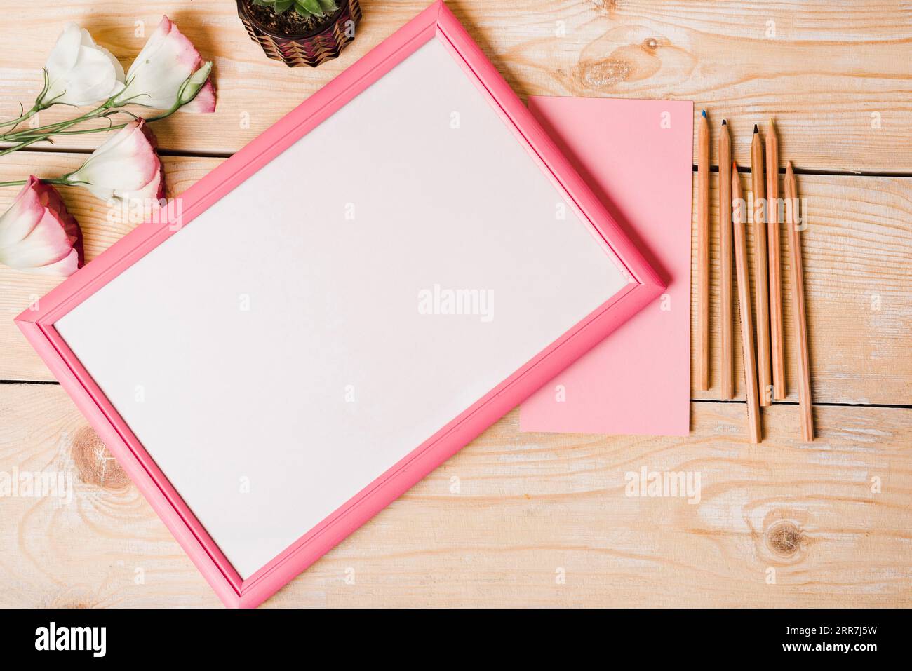 Crayons de couleur papier eustoma fleurs cadre photo blanc avec bordure rose table en bois Banque D'Images