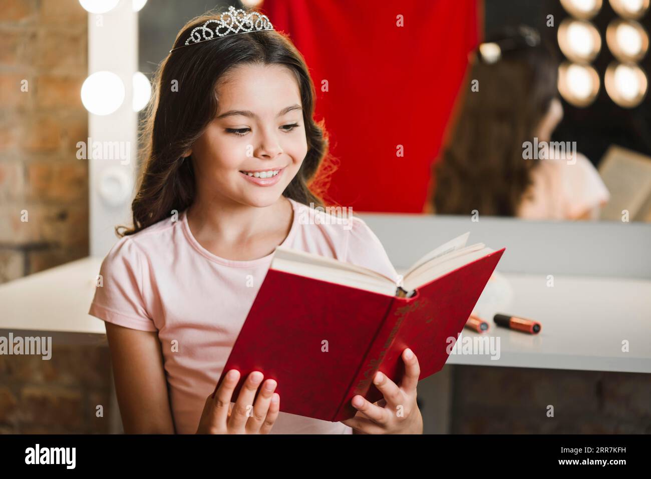 Souriante fille assise salle de maquillage livre de lecture Banque D'Images