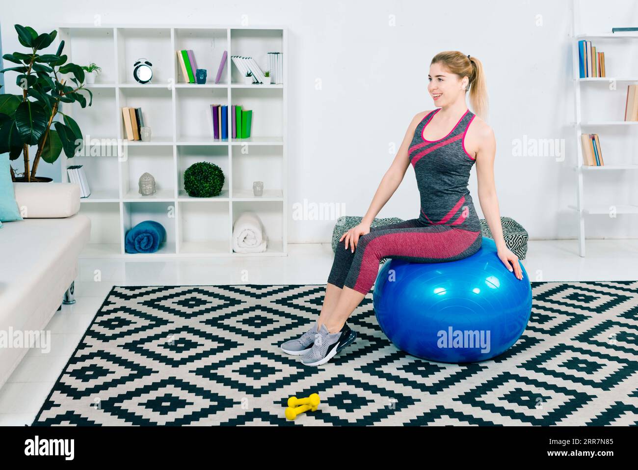 Portrait souriant fitness jeune femme assise bleu pilates ball regardant loin Banque D'Images