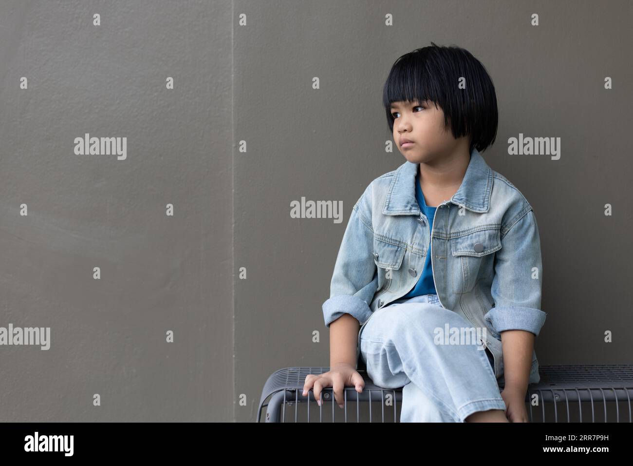Fille enfant portant un costume de jeans bleu debout avec son amie en studio. Une fille triste regardant loin sur fond de mur gris dans la maison des parents de la famille Banque D'Images