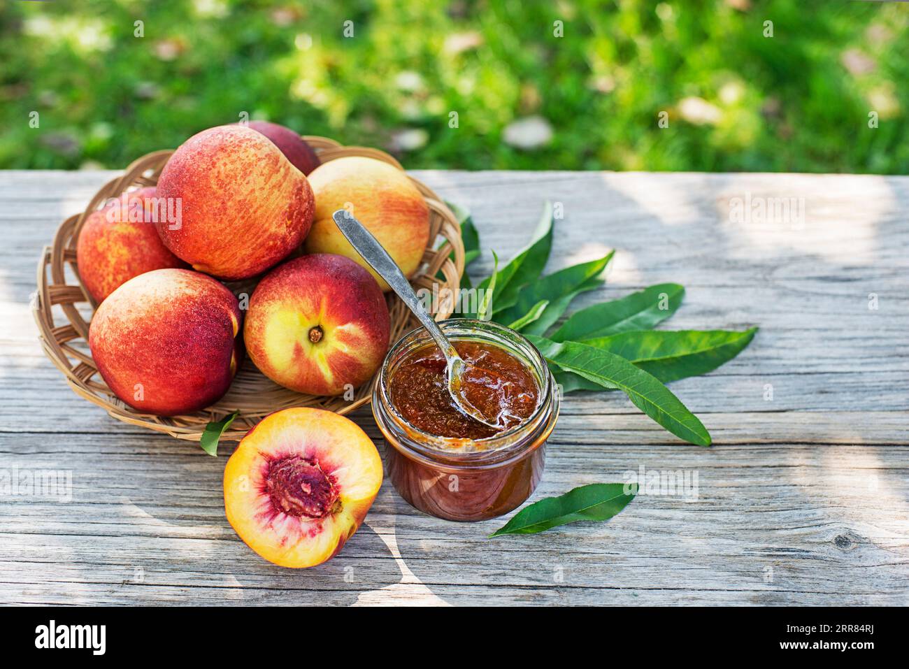 Confiture de pêche ou marmelade dans un bocal en verre avec des pêches mûres dans un panier à l'extérieur sur une journée ensoleillée Banque D'Images