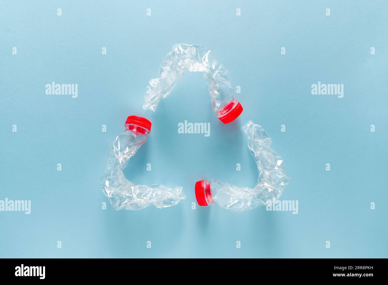 Trois bouteilles d'eau en plastique bleu pliées ensemble pour former un symbole de recyclage sur fond bleu Banque D'Images