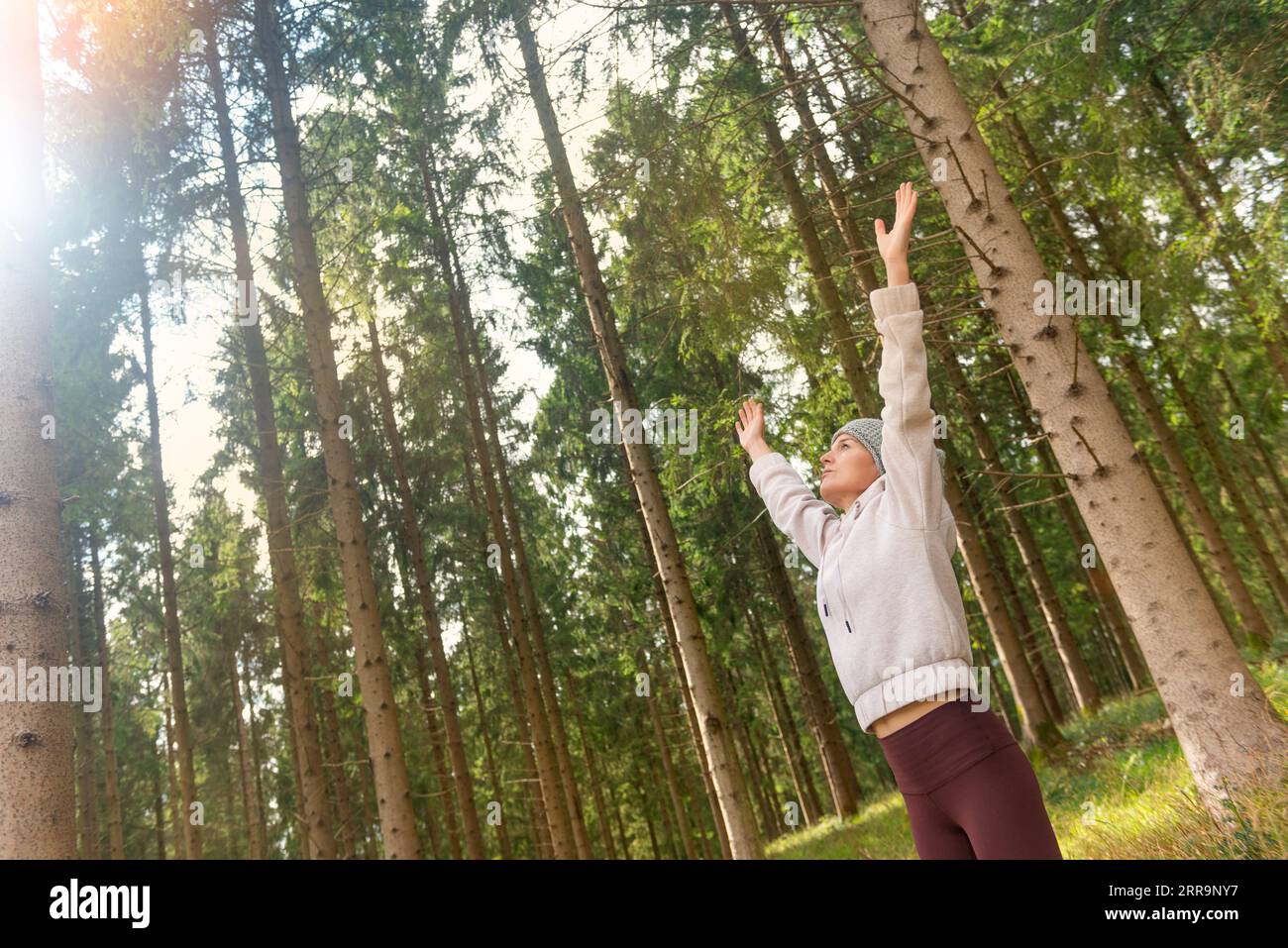 femme sportive avec ses bras levés au soleil. Exercice matinal dans une forêt. Banque D'Images