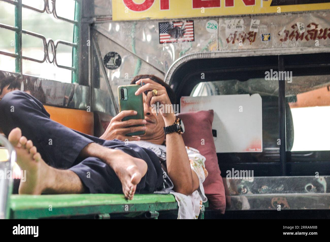 Un jeune homme adulte est assis dans un bus public, parcourant son téléphone portable avec un regard de concentration Banque D'Images