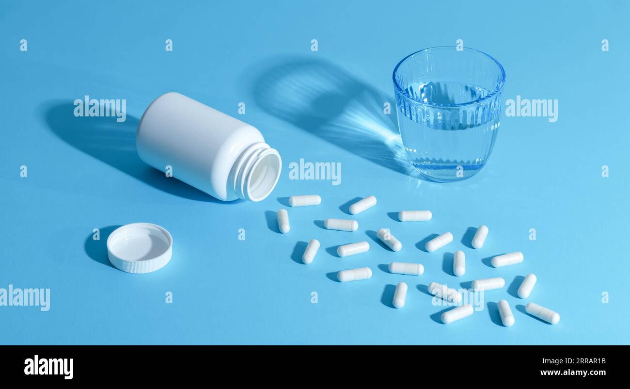 Pilules médicales blanches, capsules et verre d'eau sur un fond bleu clair. Concept de médecine. Un tas de comprimés éparpillés. Médicaments pharmaceutiques dans A. Banque D'Images