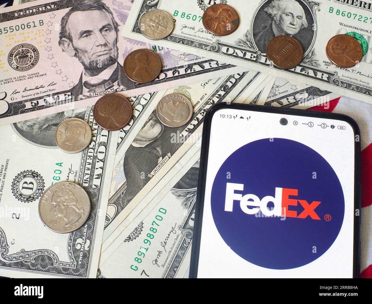 Sur cette photo, le logo FedEx Corporation est affiché sur un smartphone et des billets et pièces de monnaie américains en arrière-plan. Banque D'Images