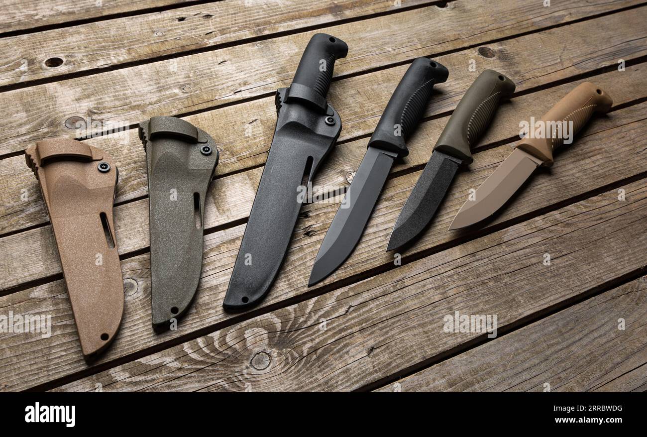 Couteaux de chasse modernes avec manches caoutchoutés et gaines en plastique. Armes de mêlée pour la chasse et l'autodéfense. Fond en bois vintage. Banque D'Images
