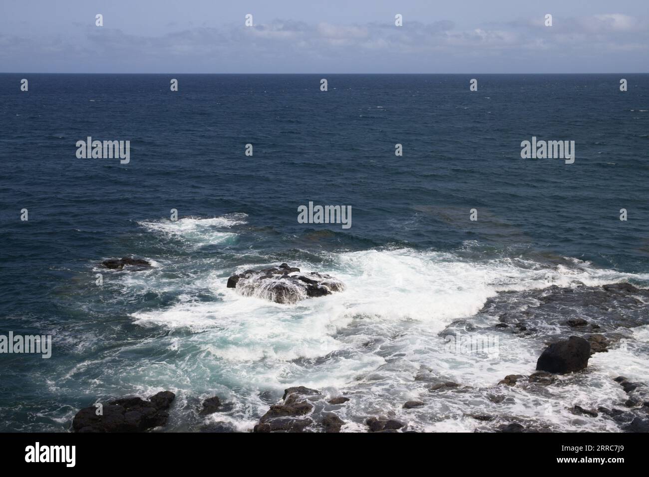 Paysage devant la mer bleue qui rencontre le ciel et dans lequel les vagues s'écrasent contre des rochers près de la côte de l'île Banque D'Images